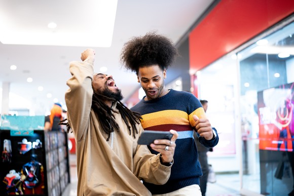 A pair of investors celebrate while looking at a cell phone while in a store.
