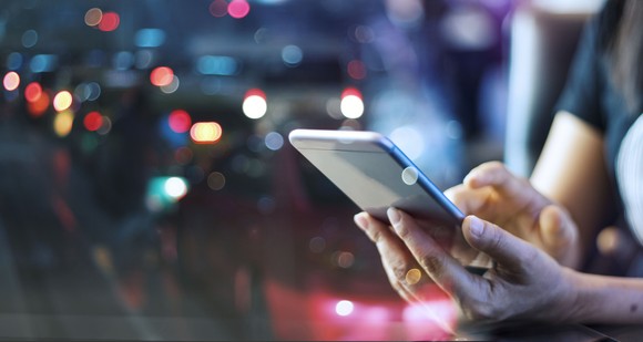 A person holding a smartphone with lights in the background.