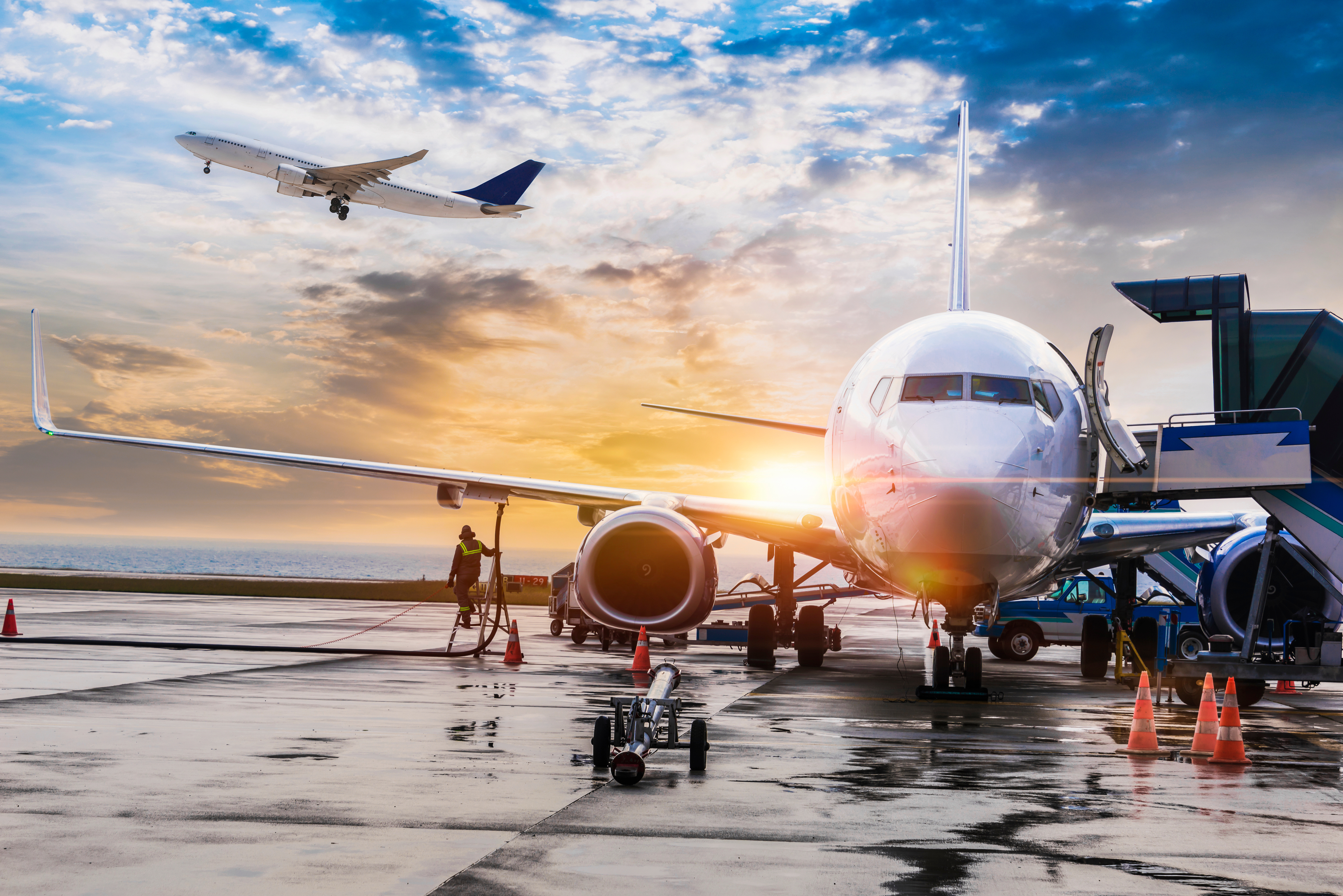 A commercial plane at a terminal gate, with another airplane taking off in the background.