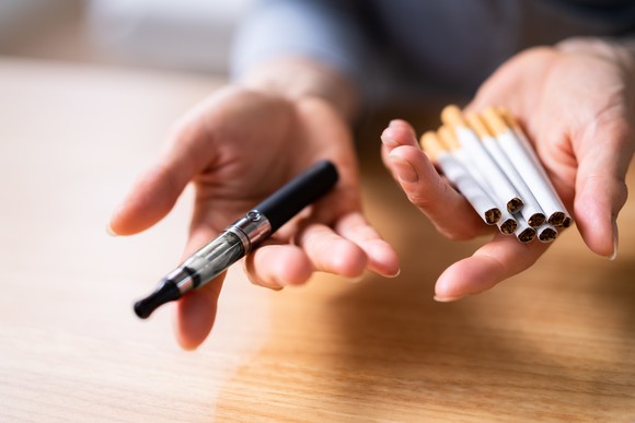 Hands holding cigarettes and a vape pen.
