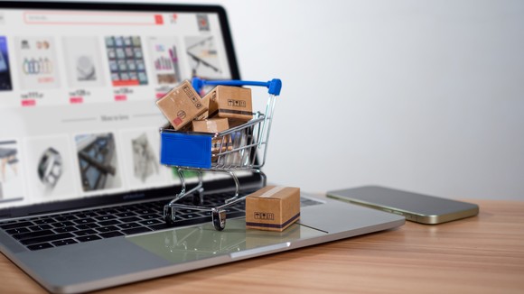 A miniature blue shopping cart full of brown packages sitting on top of a laptop computer.