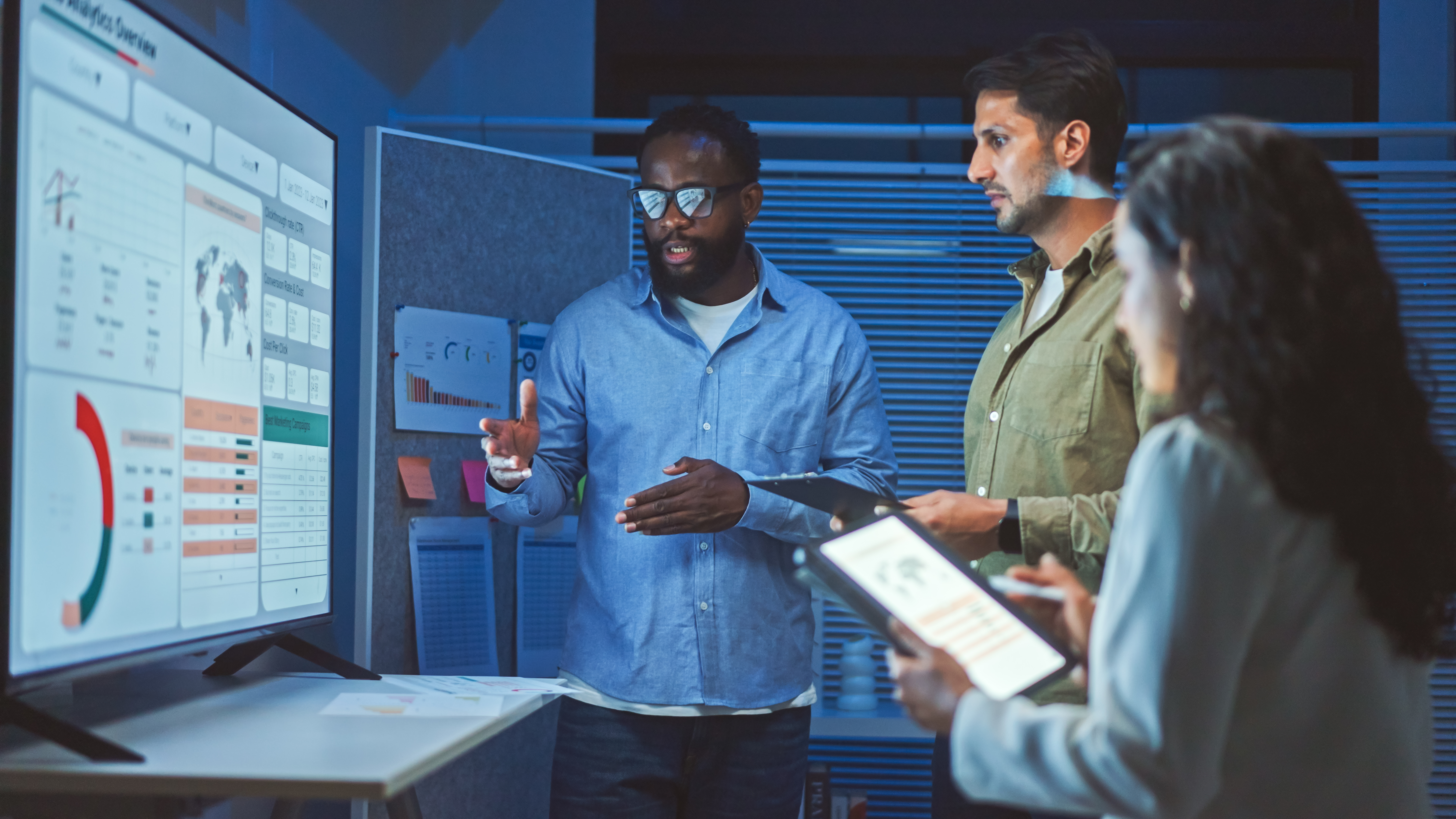 Three people look at charts on a screen.