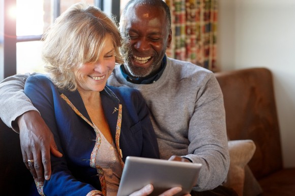 Two investors smile while looking at something on a tablet at home.