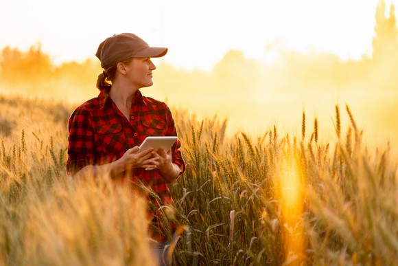 A person smiles while holding a tablet in a grassland at sunrise. 