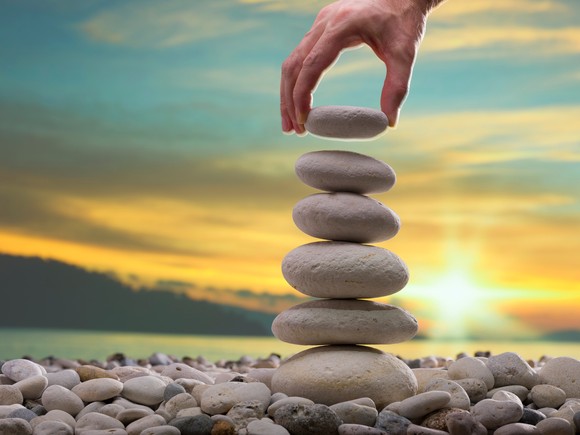 A person stacks stones into a tower with a bright sun in the background.