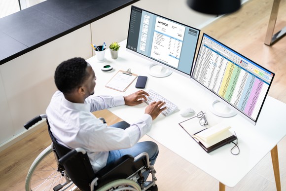 Someone typing on a keyboard while sitting in front of two monitors.