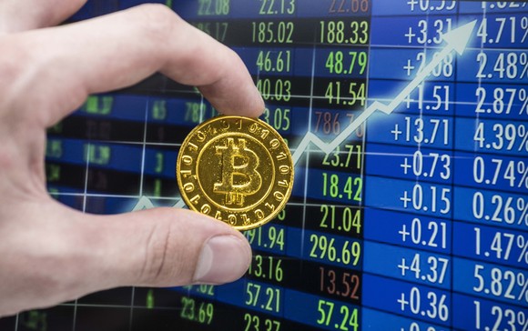 Hand holding a gold Bitcoin with an upward price arrow.
