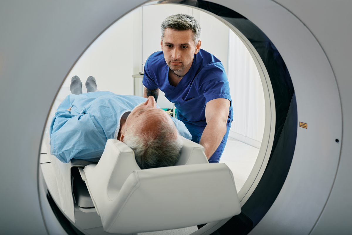 A medical technician leans over a patient going into an MRI tube.