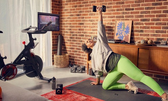 A person exercising on the floor while watching a fitness class displayed on a Peloton Bike. 