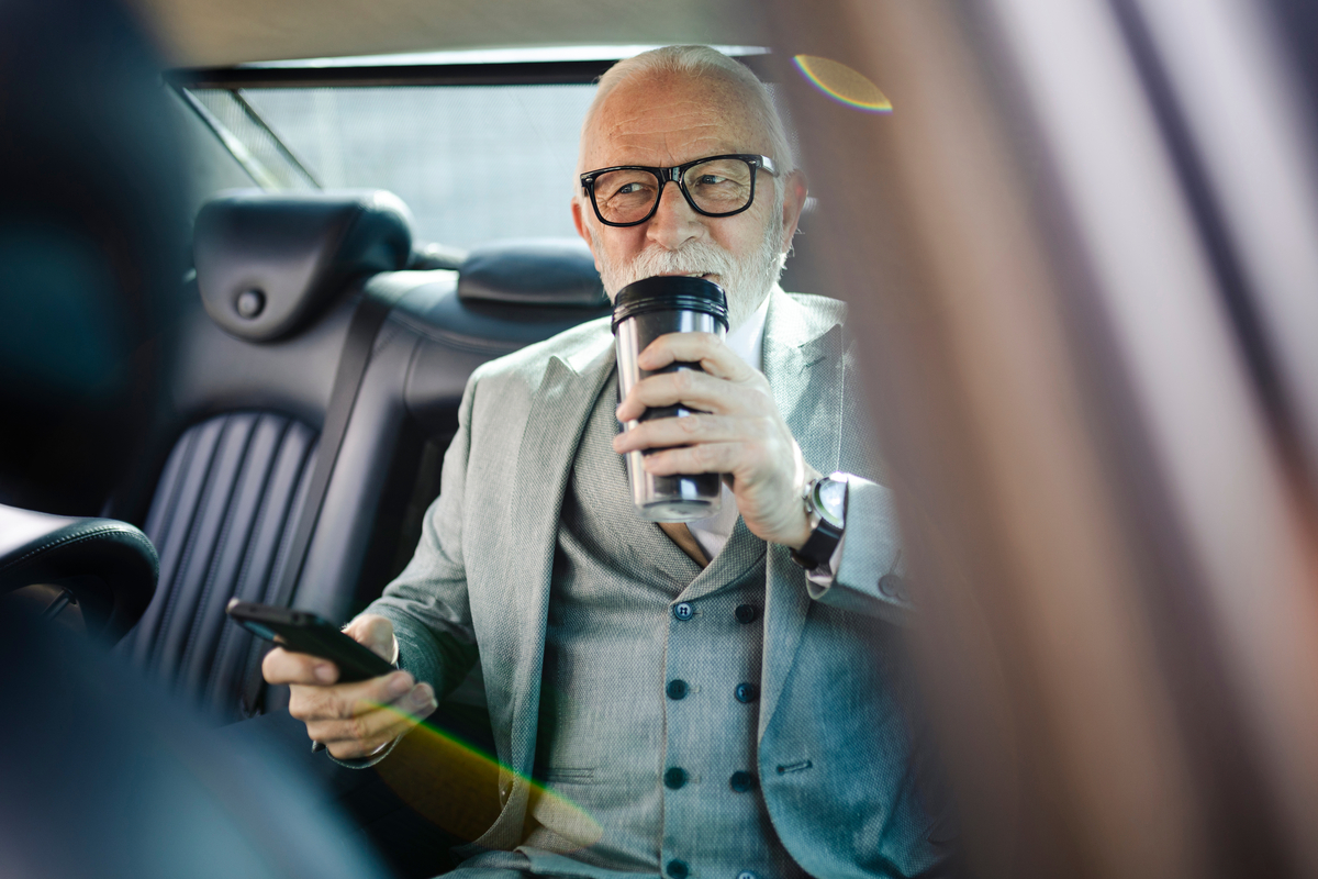 A person in the backseat of a car, drinking.