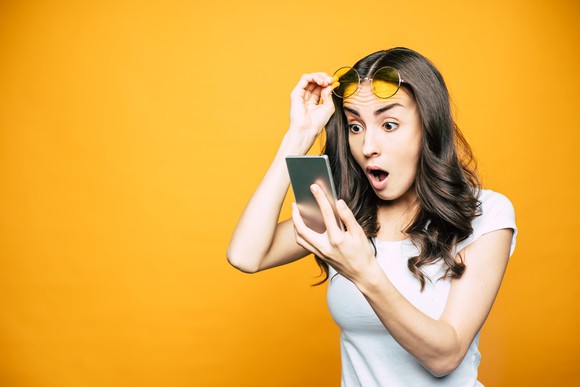Young investor looking at smartphone in disbelief. 