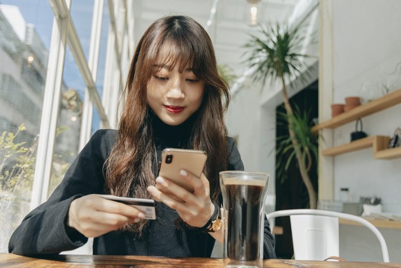 A person holds a credit card while looking at a smartphone.
