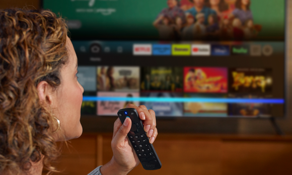 A person holding an Amazon FireStick remote while watching TV.