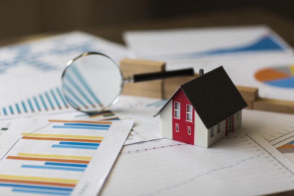 A small miniature house sits on a pile of papers.