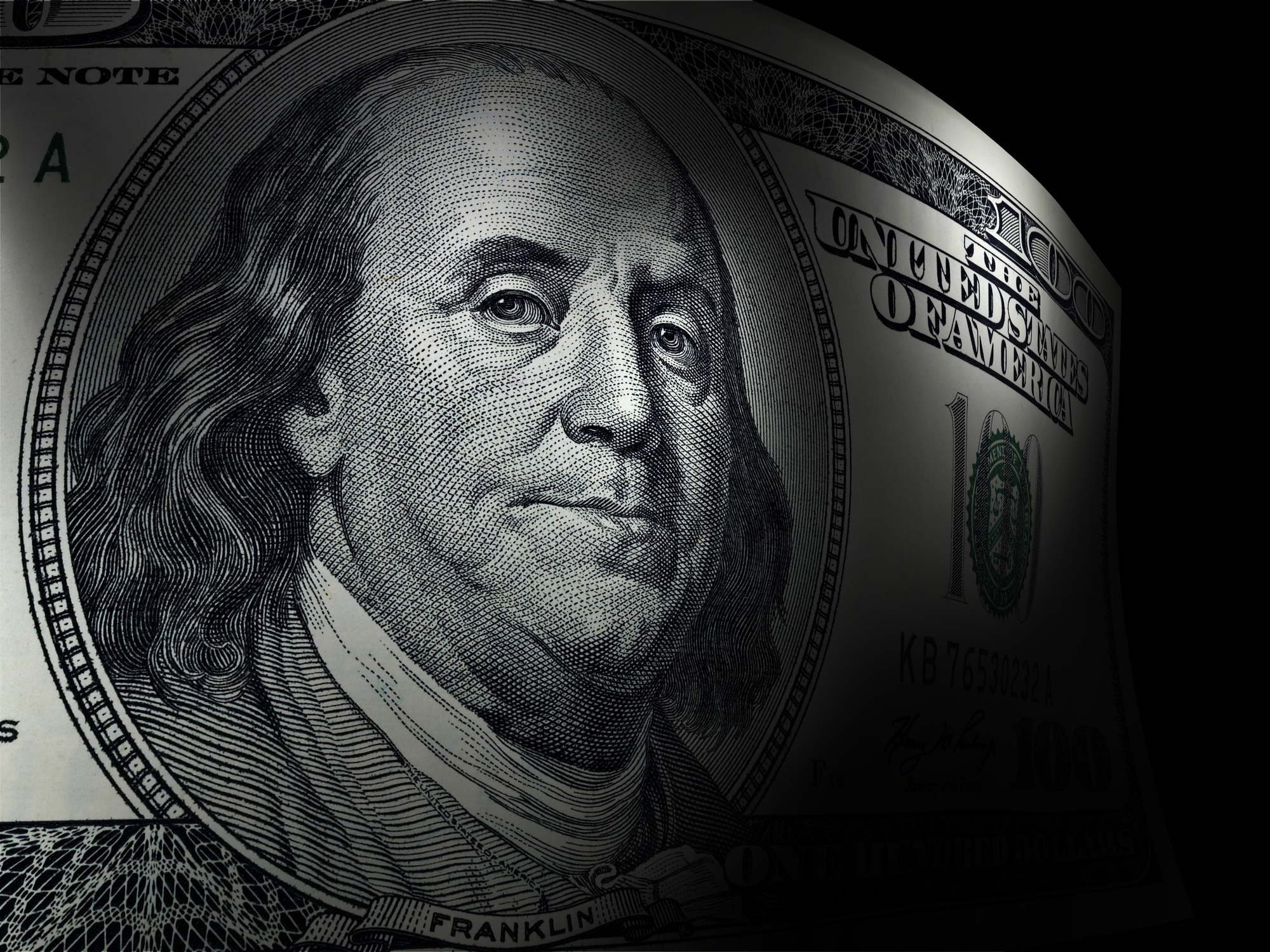 A close up of Ben Franklin's portrait on a one hundred dollar bill, with a dark background behind the bill.