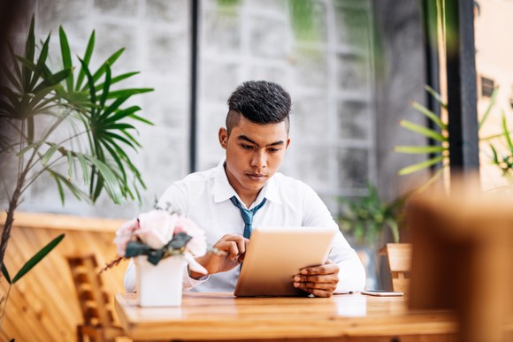 A person wearing professional attire sits at a table and interacts with a tablet. 