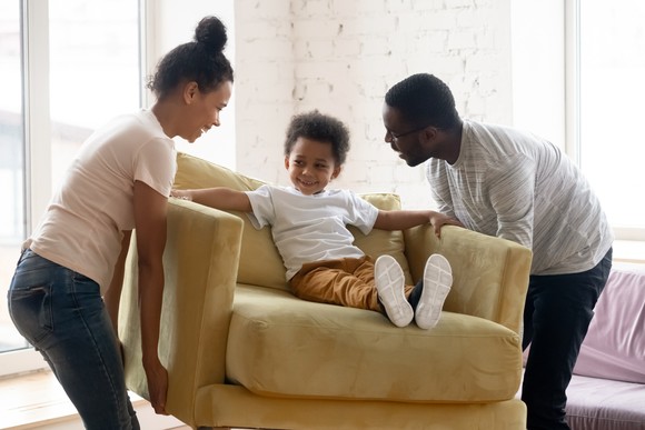Two people carrying a toddler on a loveseat.