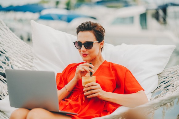 A person in a hammock while checking a laptop.