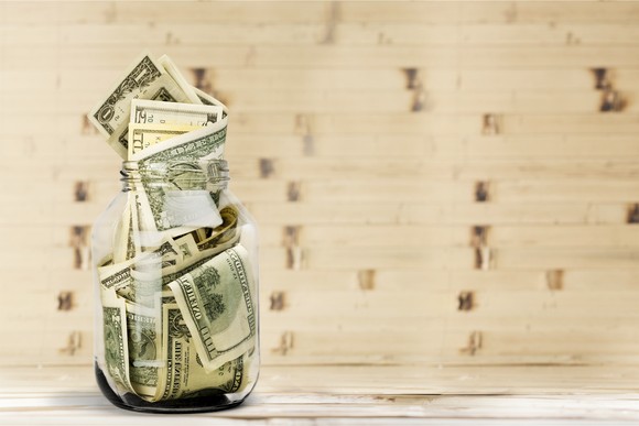 A glass jar full of different denominations in bills on a wooden table.