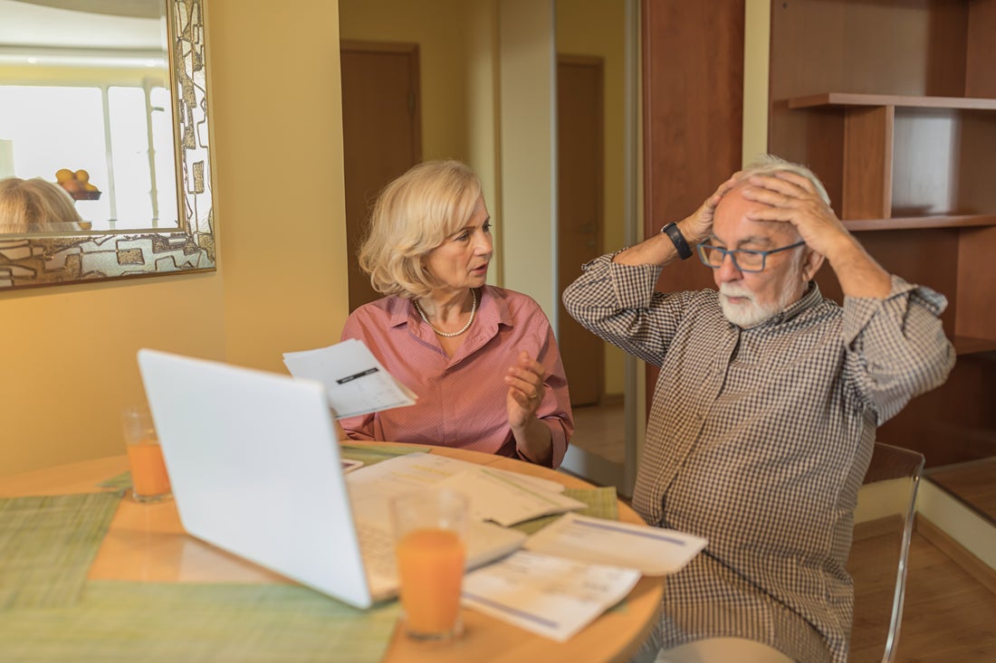Two people look at documents and a laptop at a kitchen table.