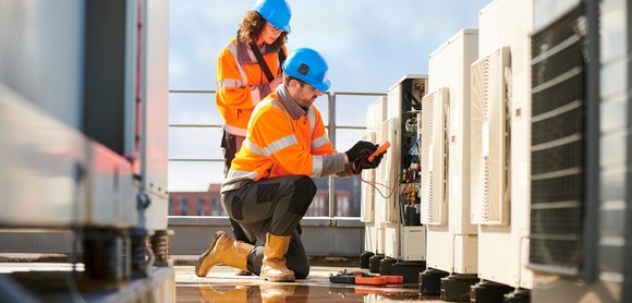 Two people wearing personal protective equipment repairing industrial equipment on a roof. 