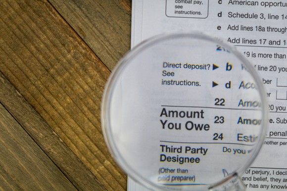 A magnifying glass laid atop a federal tax form, which has enlarged the phrase Amount You Owe.