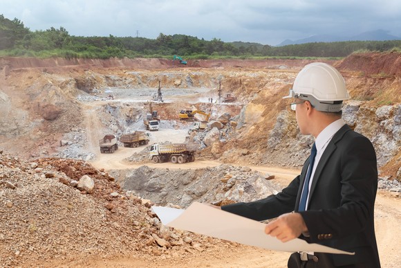 A person stands in front of a mine with a blueprint.