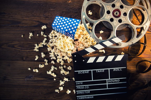 Popcorn, a movie slate, and a movie reel on a table.