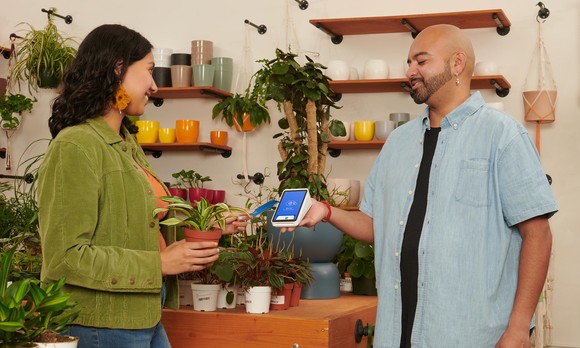 person holding up square block device for customer to use to purchase an item.