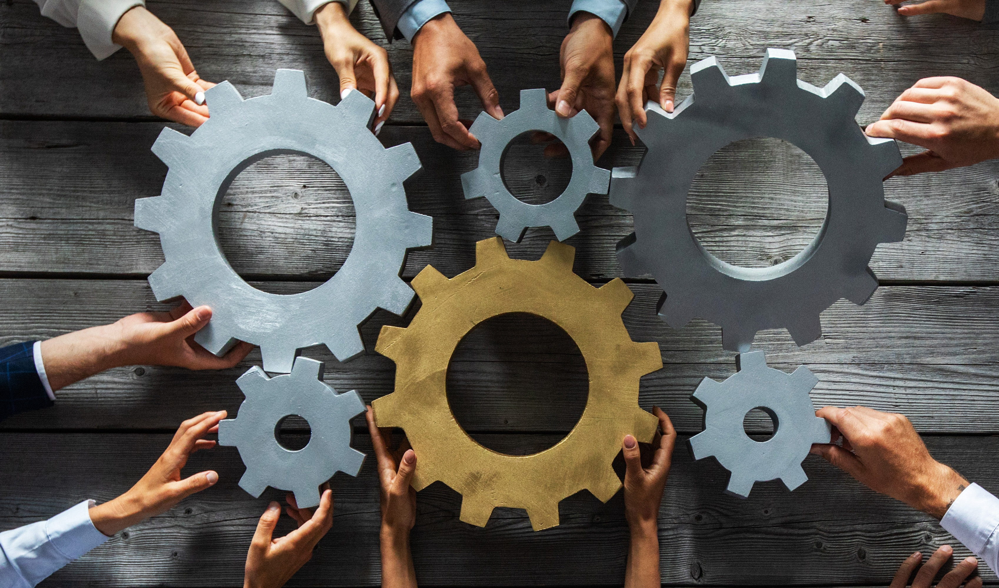 Several hands holding an assortment of gears that fit together.