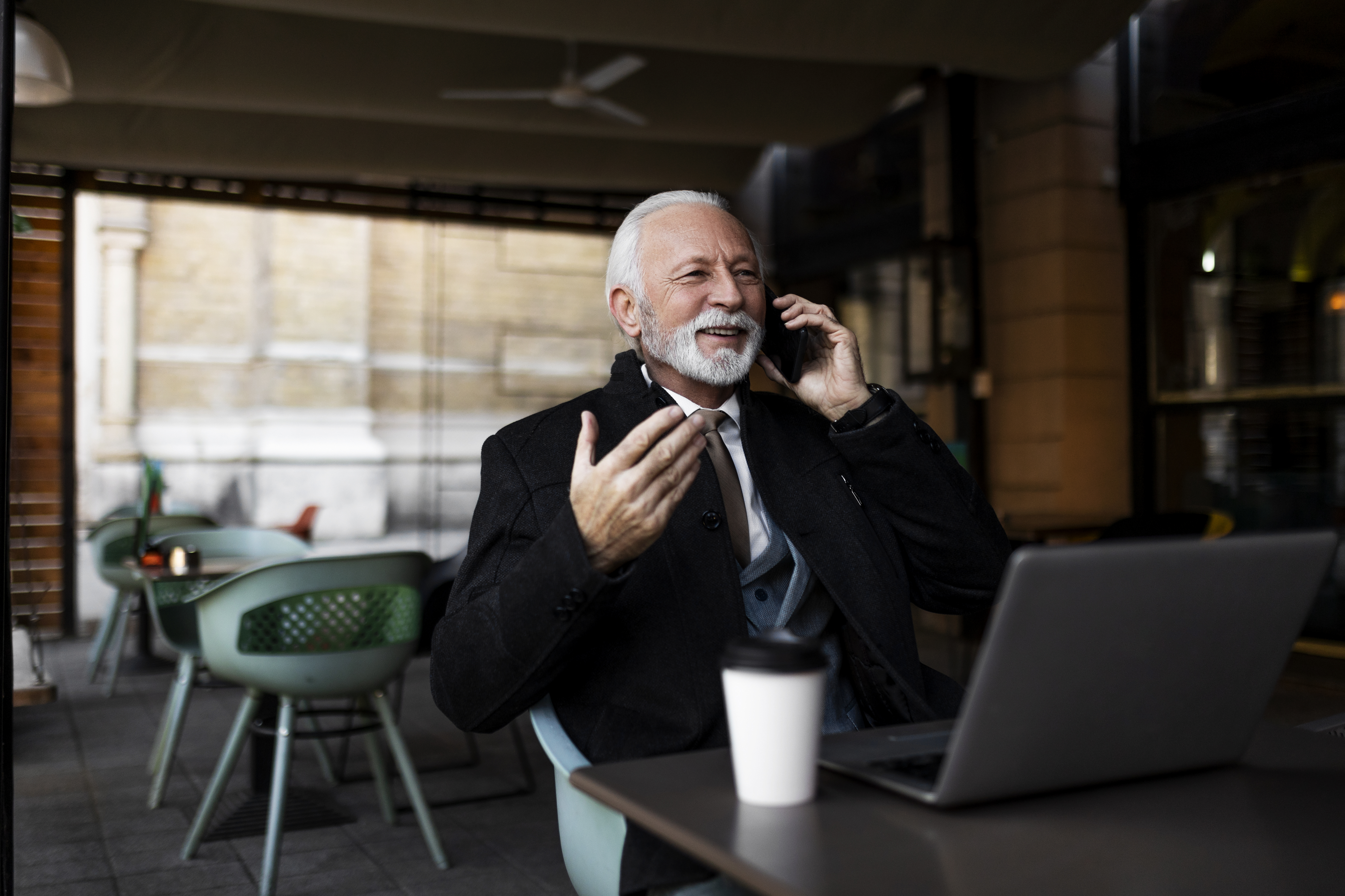 Someone sitting at a restaurant table in front of a laptop while talking on the phone.