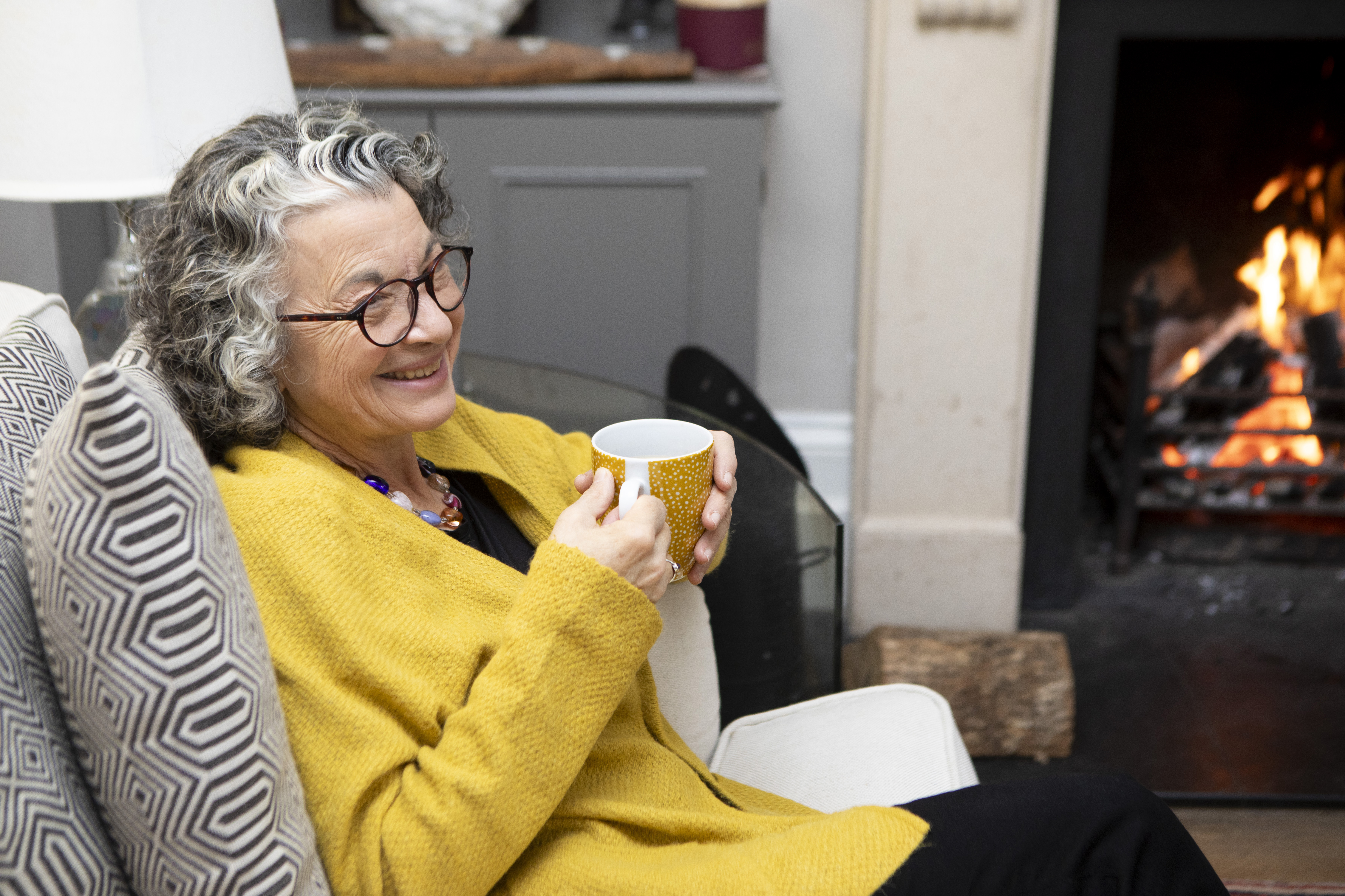 Person sitting by a fire with a mug in hand.