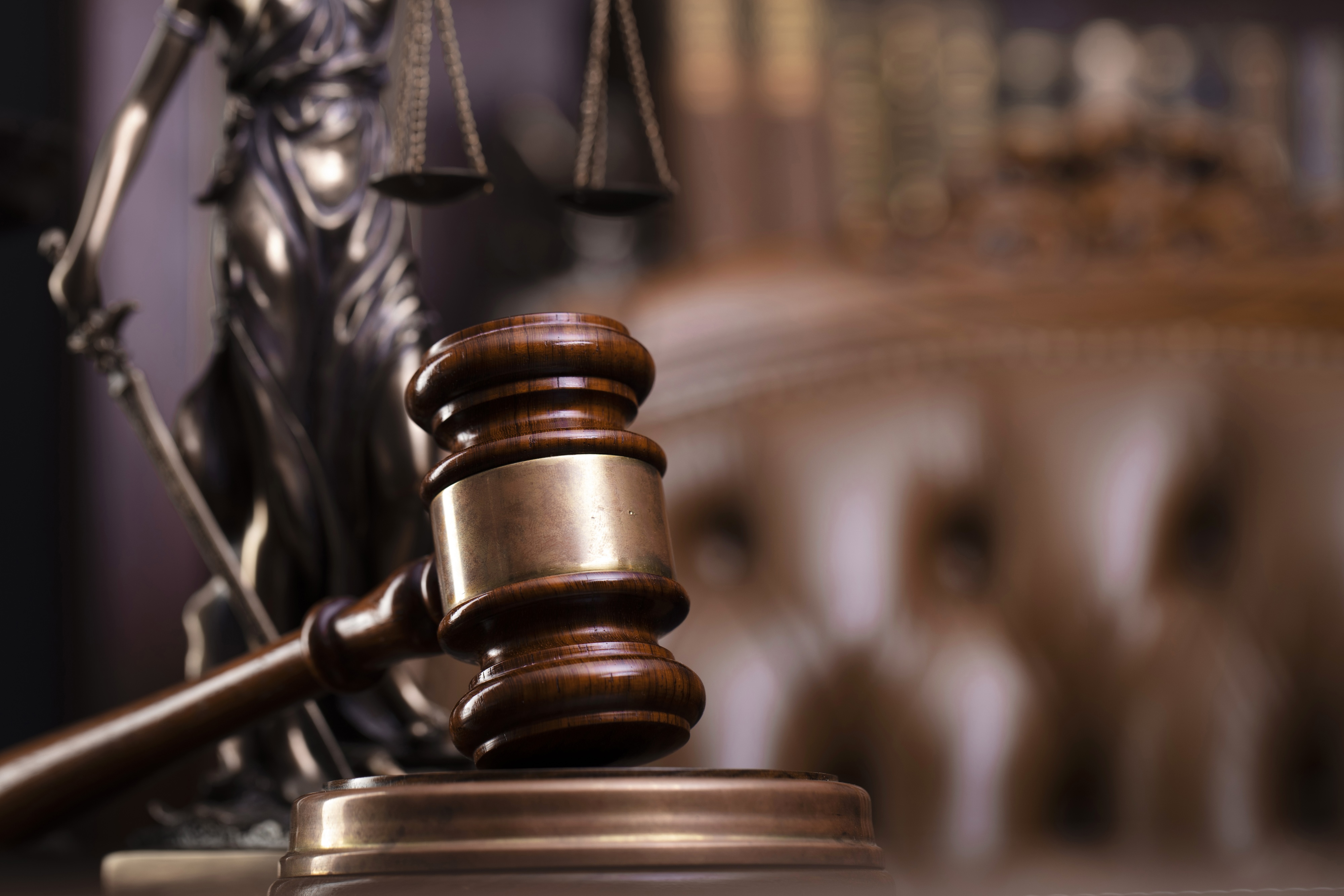 A gavel in a courtroom with Lady Justice in the background.