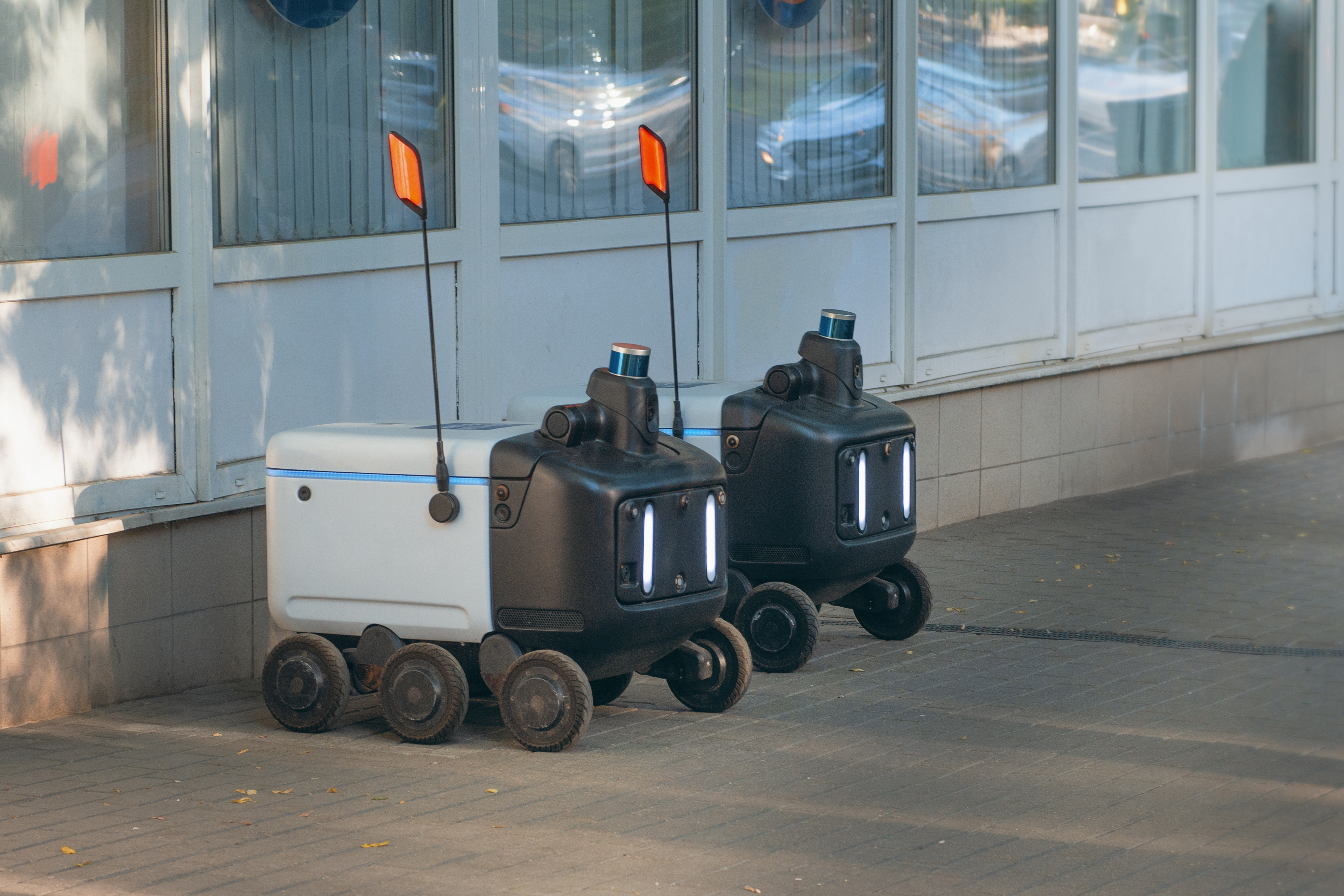 A pair of autonomous food delivery robots waiting on the sidewalk