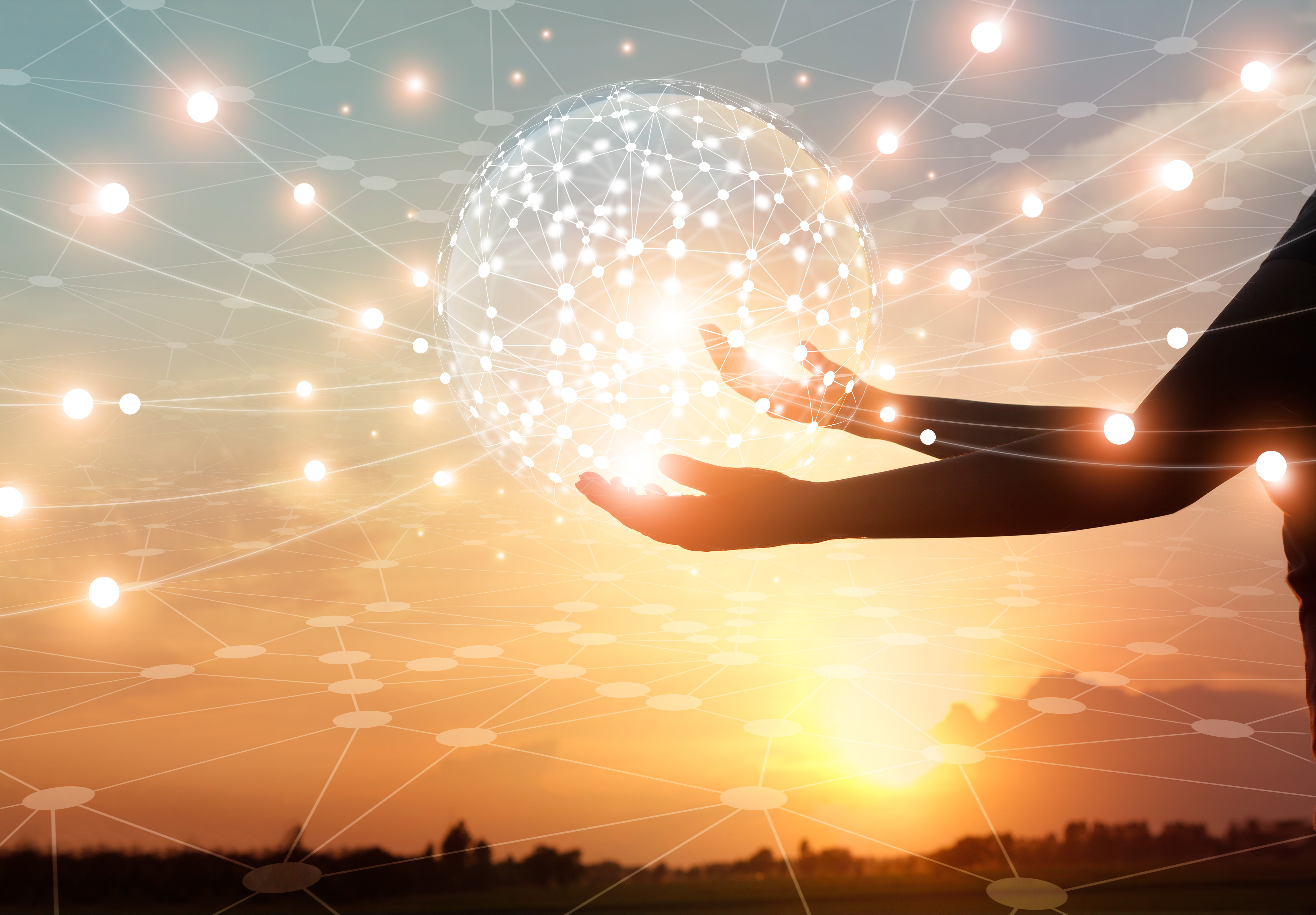Silhouette of hands holding a sphere of interconnected dots of light against a sunset or sunrise crossed by orbs of light.