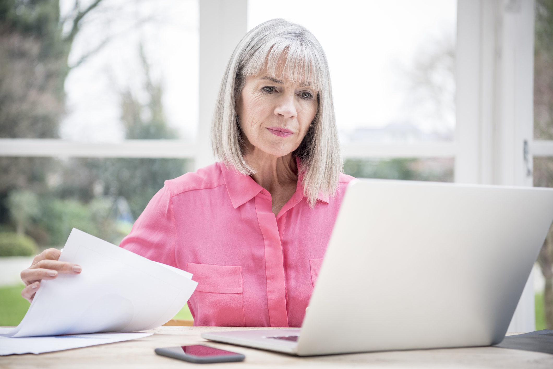 Serious person holding document and looking at laptop.