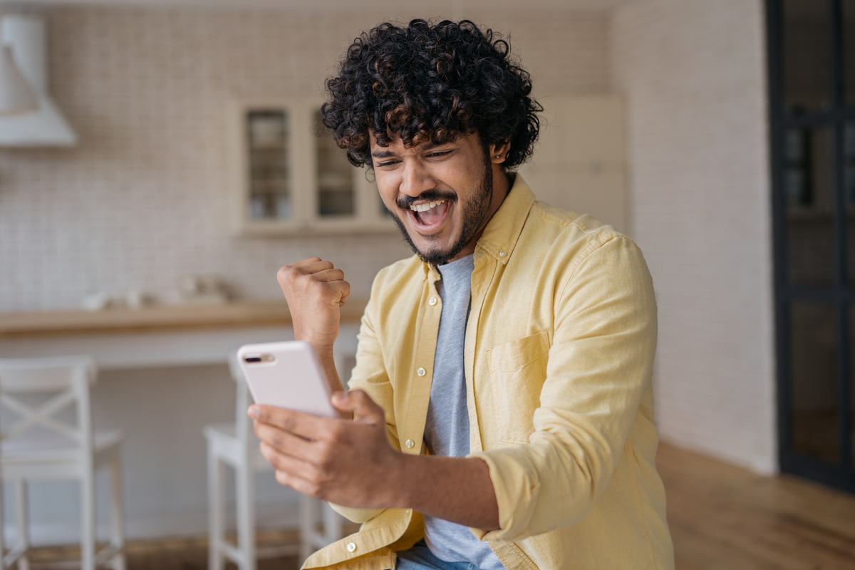 excited man celebrates while looking at smartphone.