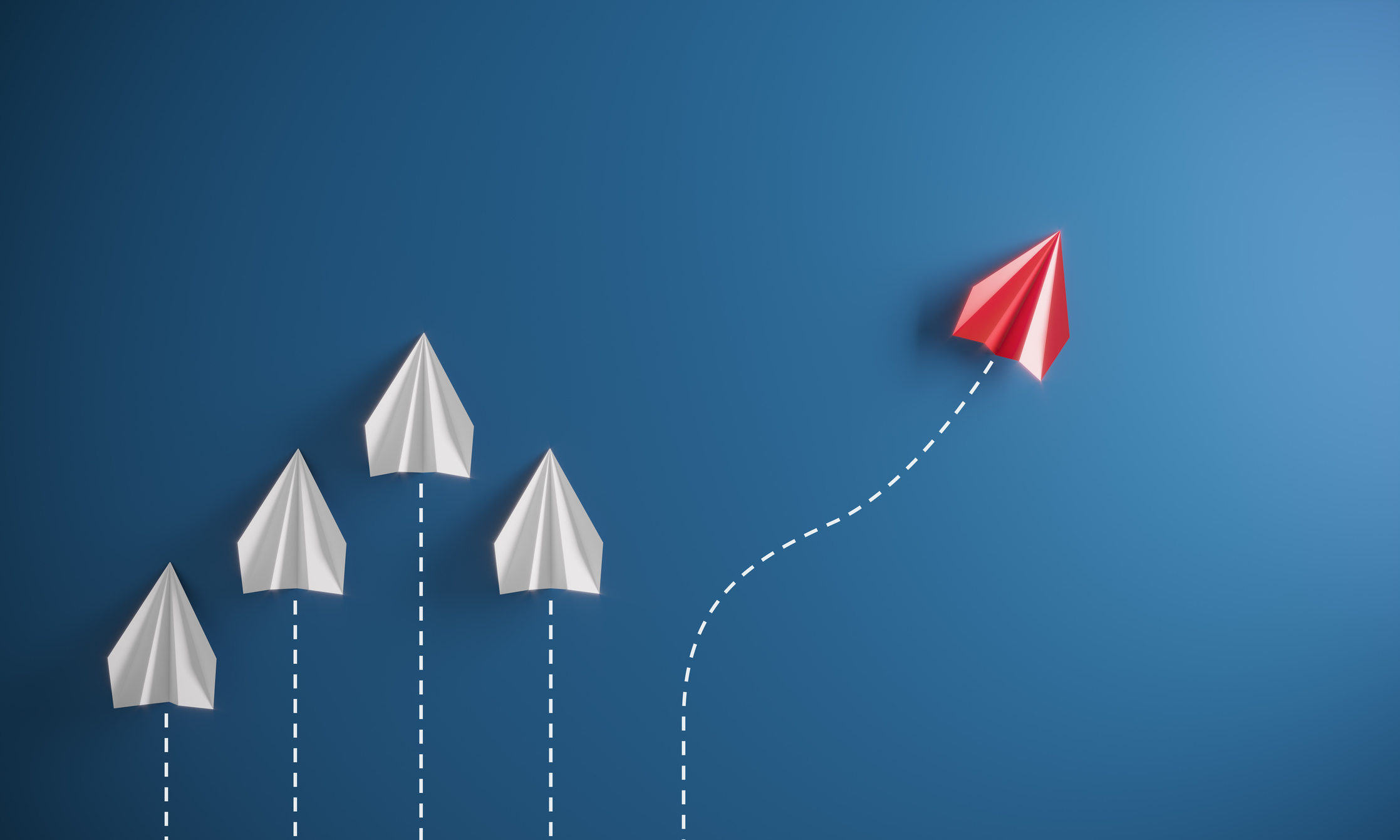 A red paper airplane taking a different path than four white paper airplanes.