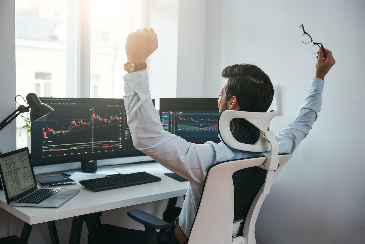 happy trader looks at financial charts on computers.