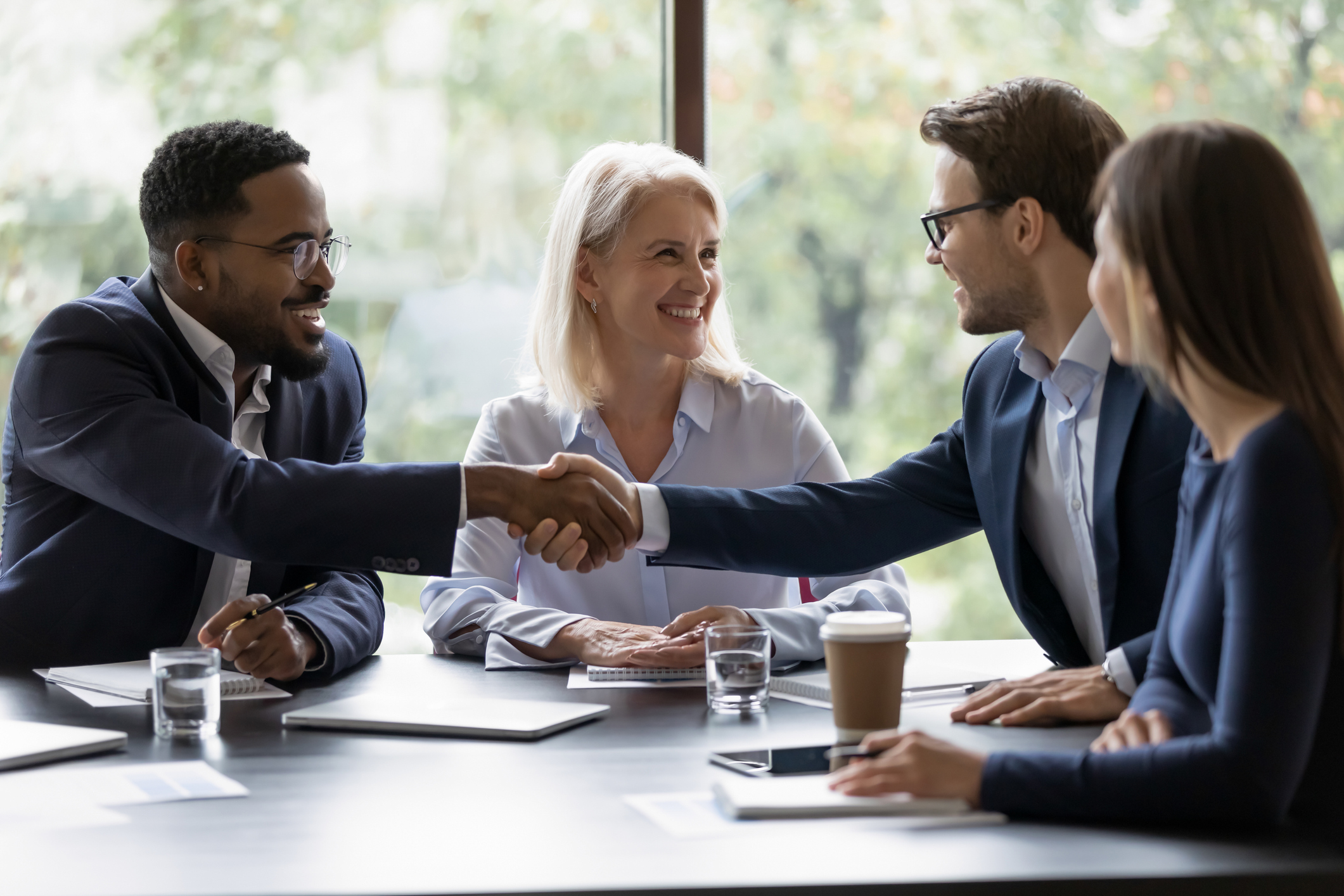 Two_businessmen_shaking_hands_in_a_team_meeting