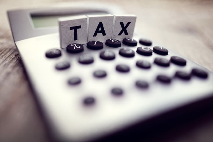 Three tile letters spelling TAX on top of a calculator