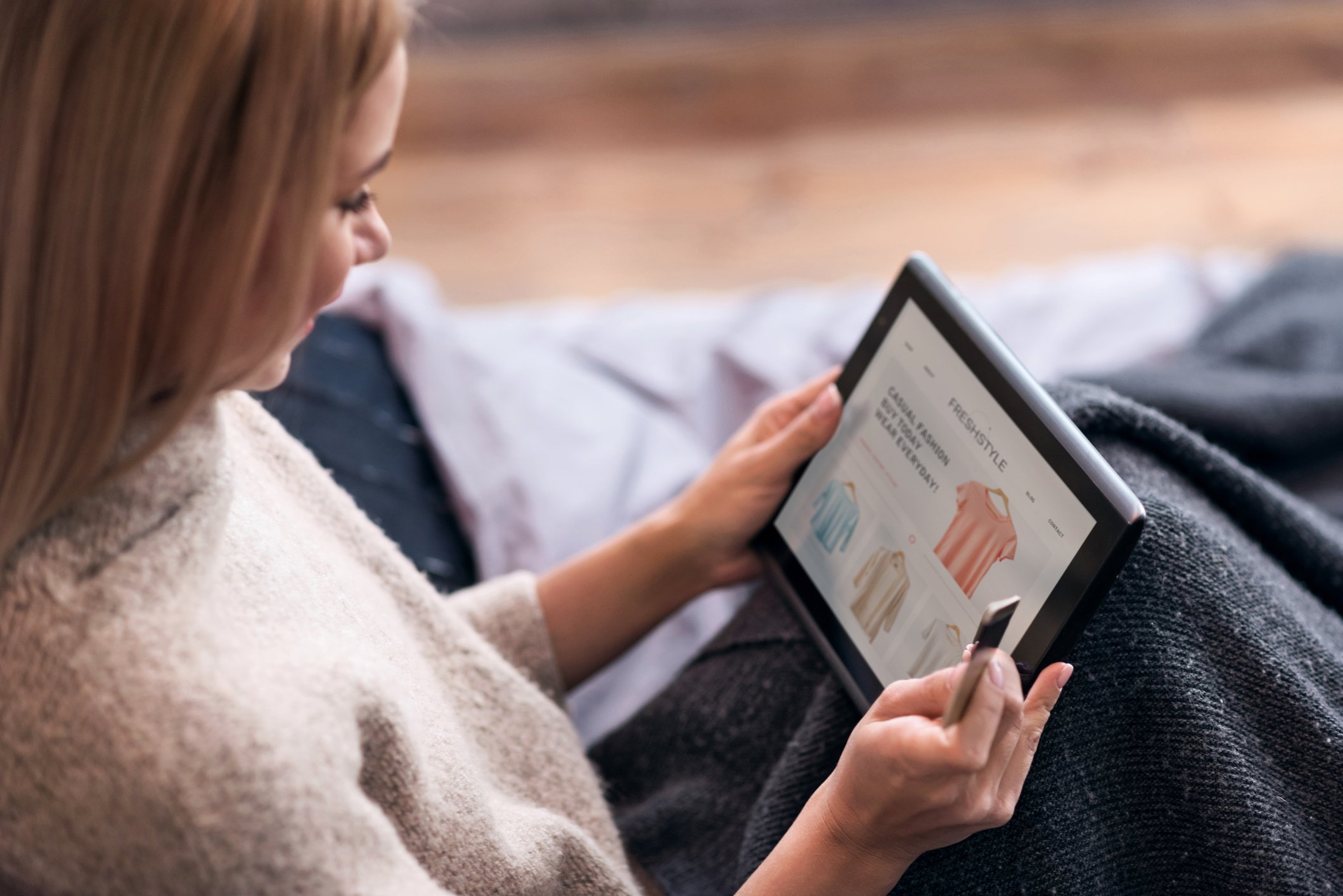 A woman shops online on her tablet while in bed.