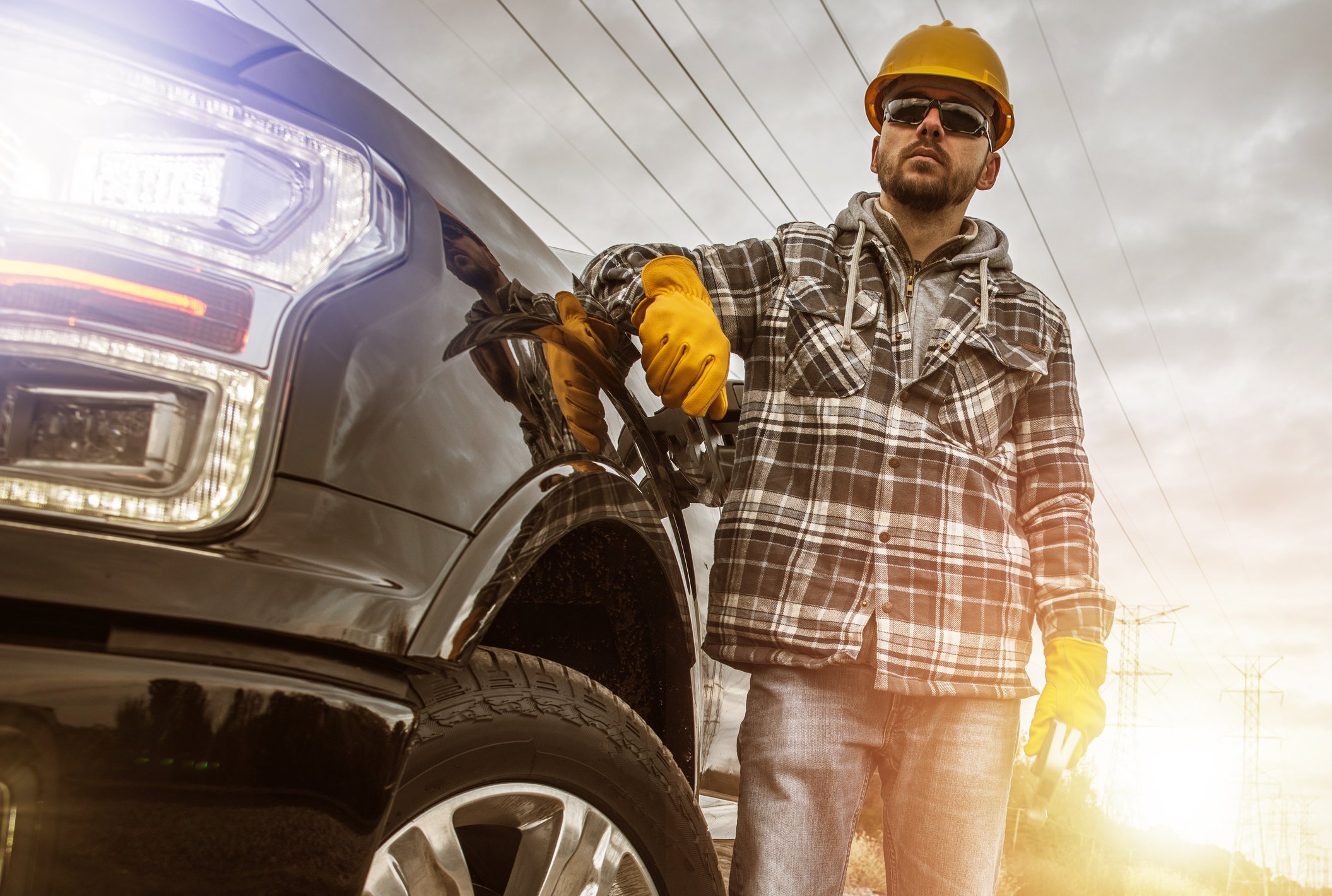 A contractor in a hard hat standing next to a pick-up truck with the lights on