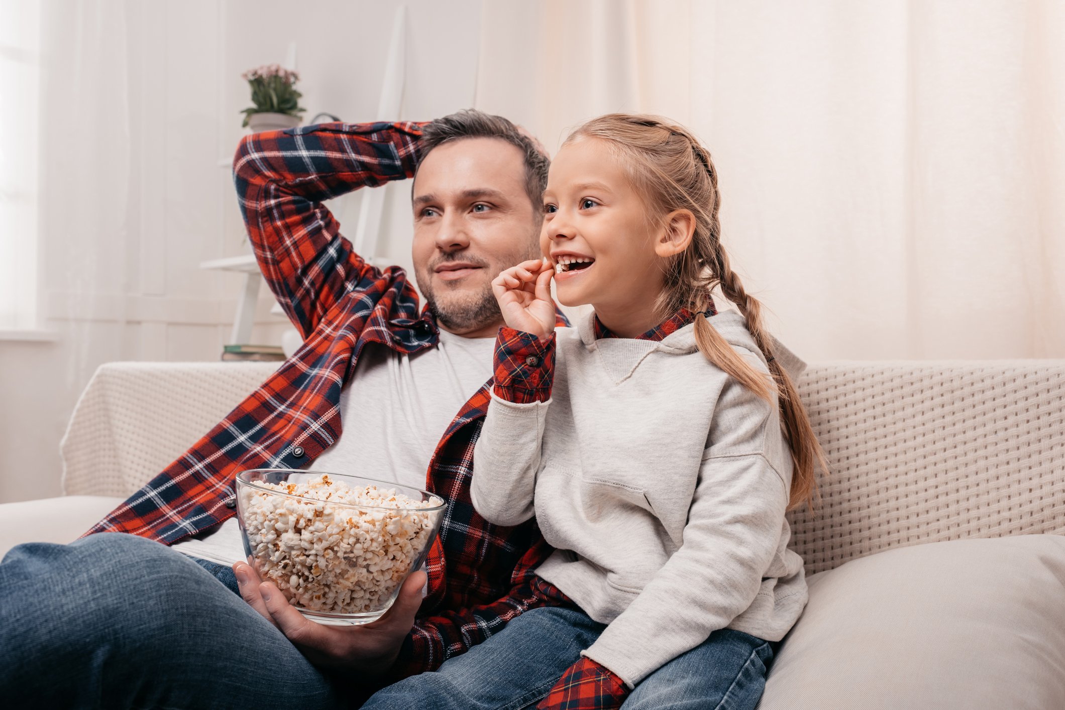 A father and daughter watching TV on the couch with popcorn