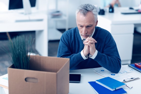 Older man sitting pensively at work, with a cardboard box on his desk