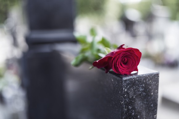 A rose lies on top of a headstone.