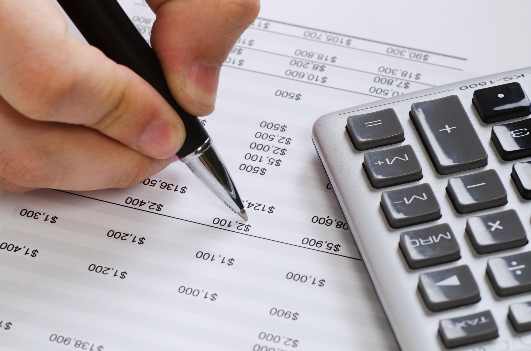 A close-up of someone marking a balance sheet with a pen, and a calculator nearby