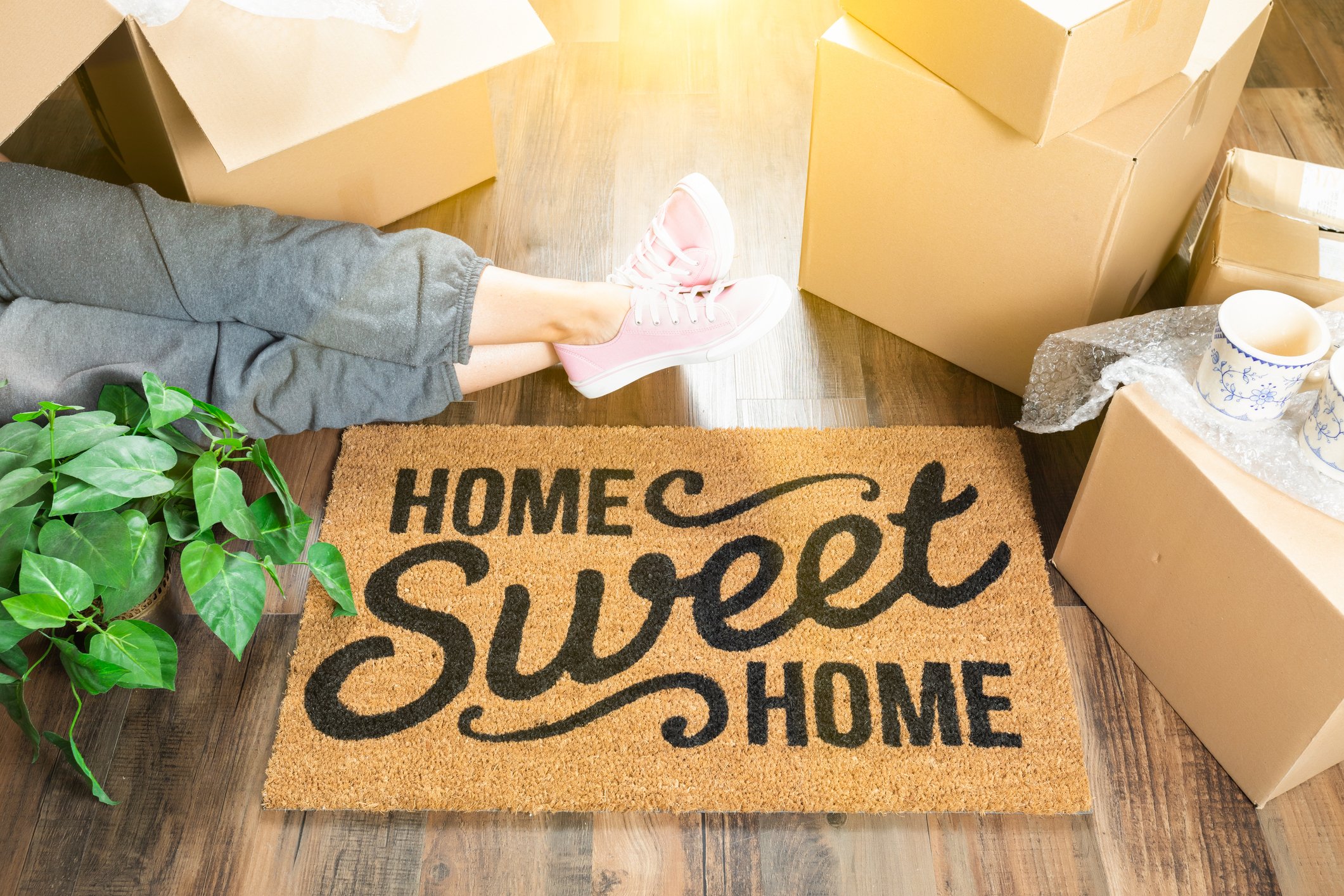 Woman's legs stretched out, surrounded by moving boxes and a Home Sweet Home doormat.