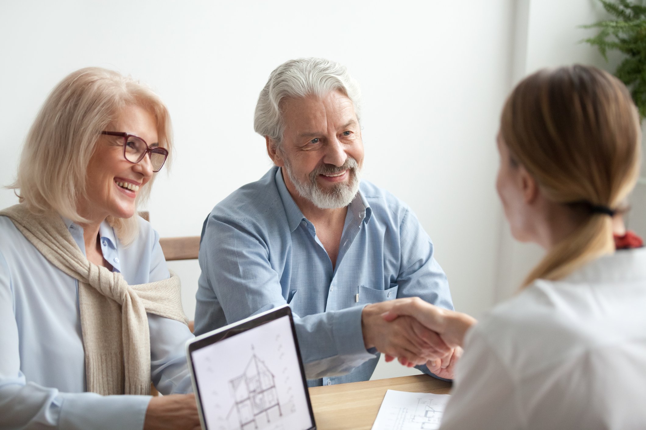 A mature couple shake hands with a financial planner.