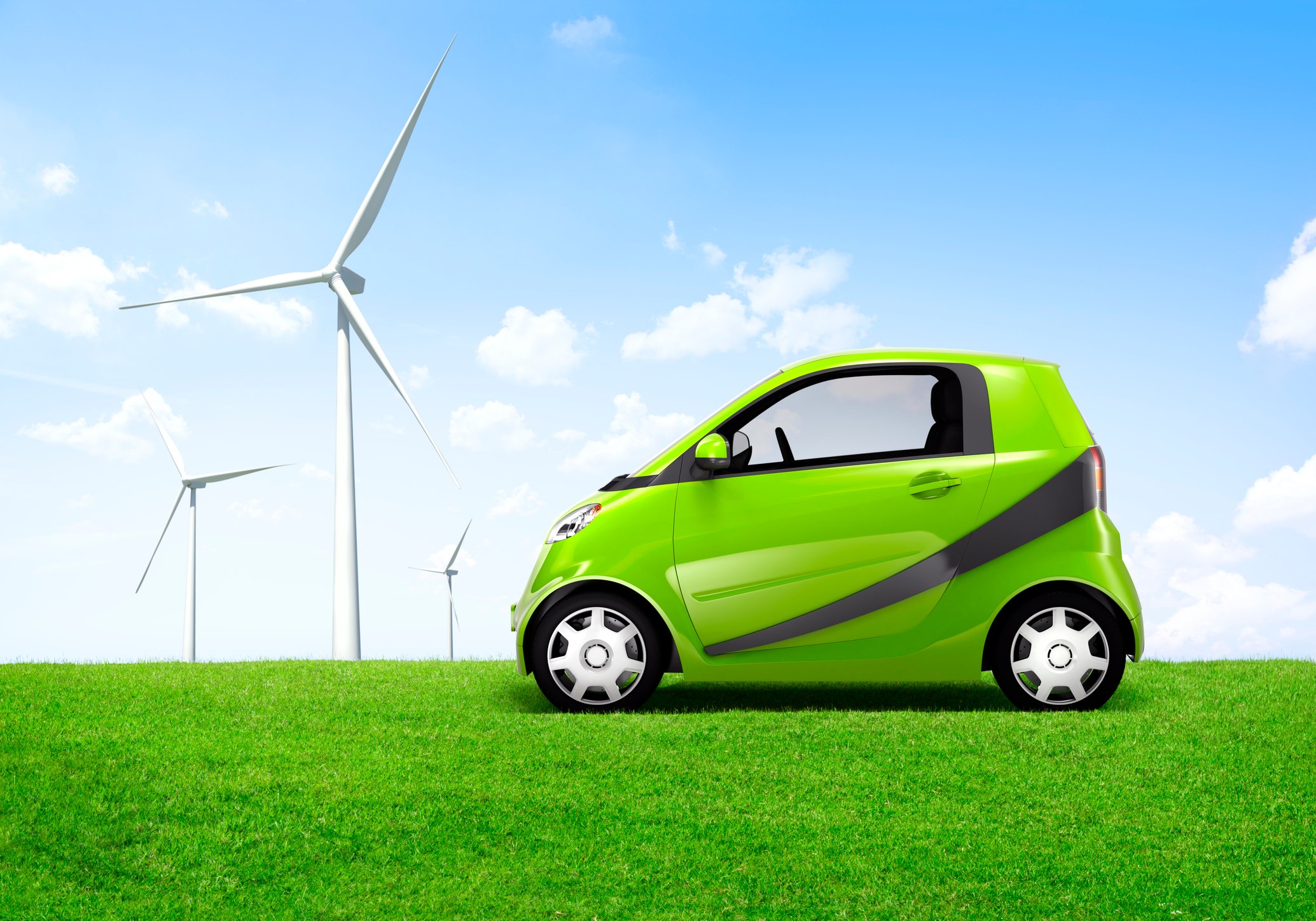 A compact green electric car in a field with windmills in the background.
